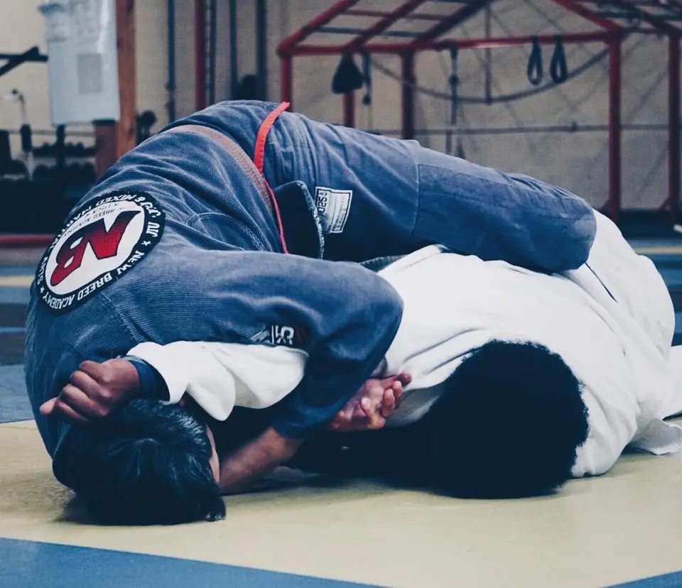 Two students training Brazilian Jiu-Jitsu in gis on the mat