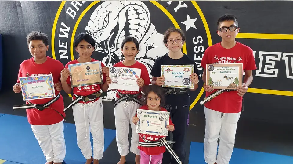 Kids in gis holding their promotion certificates in front of the New Breed logo