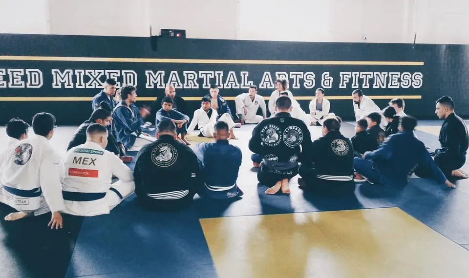 Students seated on the mats in front of the New Breed Mixed Martial Arts & Fitness banner